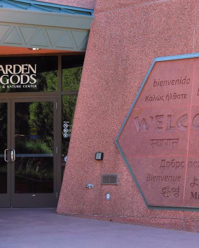 The image shows the entrance to a building with a large glass door and a distinctive hexagonal stone sign on the wall to the right.