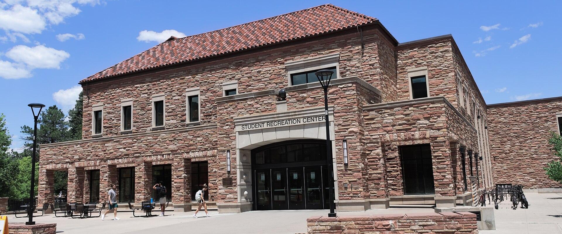 A large, two-story stone building with a red tile roof, identified by a sign above the main entrance as the "STUDENT RECREATION CENTER".