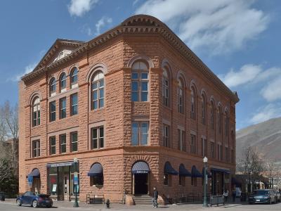 A three-story reddish-brown sandstone building on a street corner with blue awnings, featuring a sign above the entrance that reads "WHEELER OPERA HOUSE" and another sign for "Aspen's Shop".