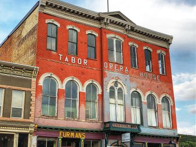 A red brick Italianate-style building with "TABOR OPERA HOUSE" painted in large white letters on the facade, featuring arched windows, a balcony, and storefronts at street level including "FURMAN'S".