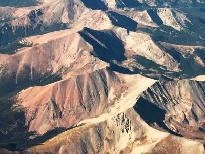 An aerial photograph showing rugged, multi-colored mountain ridges with exposed earth and rock formations, likely taken from an aircraft.