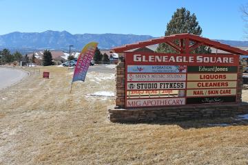 A large outdoor commercial sign for "Gleneagle Square" listing businesses like Studio Fitness and Mig Apothecary, with mountains in the background.