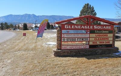 A large outdoor commercial sign for "Gleneagle Square" listing businesses like Studio Fitness and Mig Apothecary, with mountains in the background.