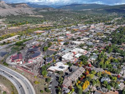 An aerial view of a town nestled in a valley with mountains in the background, featuring a prominent red brick roundhouse and rail yard in the lower left foreground.