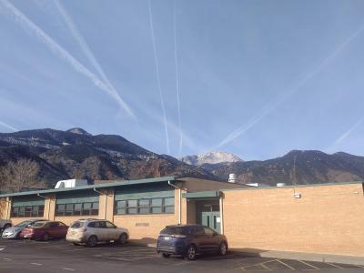 A single-story brick school building with a parking lot in the foreground and a large mountain range in the background.