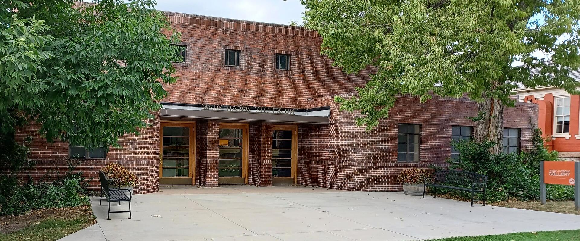 A single-story red brick building with a flat roof, featuring an entrance canopy labeled "MARY HARRIS AUDITORIUM" and a freestanding orange sign on the lawn reading "COLORADO GALLERY".