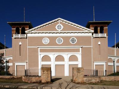 A large, historic wooden building with a distinctive white roof and multiple cupolas, situated on a hillside with mountains in the background.