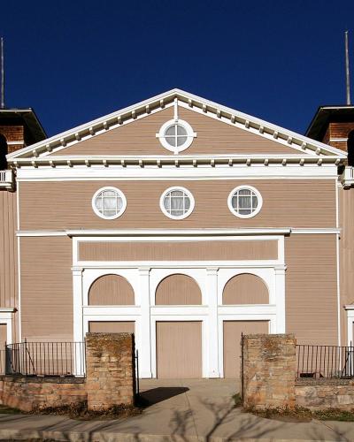 A large, historic wooden building with a distinctive white roof and multiple cupolas, situated on a hillside with mountains in the background.