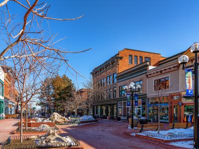 A brick-paved pedestrian mall lined with historic brick buildings, bare trees, benches, and snow piles under a clear blue sky.