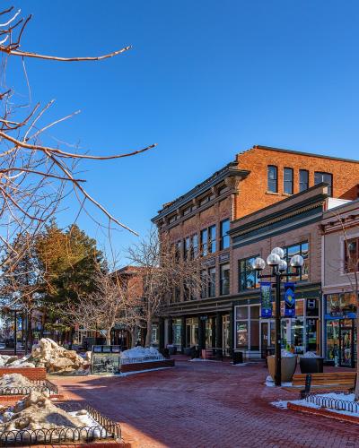 A brick-paved pedestrian mall lined with historic brick buildings, bare trees, benches, and snow piles under a clear blue sky.