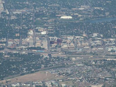 An aerial view of a city skyline with a large white domed stadium and a lake in the background, taken from a high elevation.