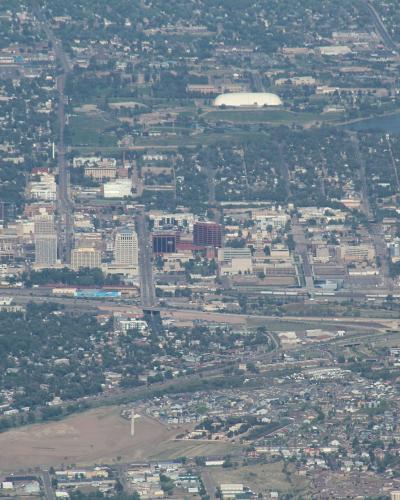 An aerial view of a city skyline with a large white domed stadium and a lake in the background, taken from a high elevation.