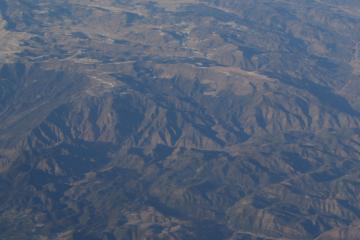 An aerial photograph showing a vast, rugged mountain landscape with deep valleys and ridges, likely taken from an aircraft.