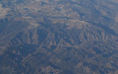 An aerial photograph showing a vast, rugged mountain landscape with deep valleys and ridges, likely taken from an aircraft.